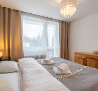 Ložnice v rekreačním apartmánu s manželskou postelí a komodou, okno s výhledem.