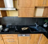 Kuchyňská linka v 2-pokojovém bytě, s podlahou s dřevěným dekorem a tmavými obklady.