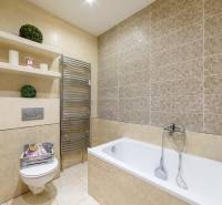 Koupelna se sprchou, vanou a poličkami v 2-pokojovém bytě s neutrálními obklady.