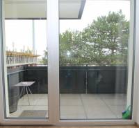 Balkon s posuvnými dveřmi a výhledem na stromy v 1-pokojovém bytě na Broskvoňové v Rovince.