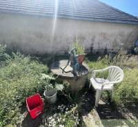 Zahrada v Jatove s pumpou, plastovou židlí a kbelíkem u rodinného domu.