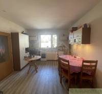 Kuchyně v rodinném domě s dřevěným dekorem podlahy, jednoduchý nábytek a jídelní stůl.