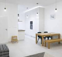 Interiér 2-pokojového bytu s bílými stěnami, dřevěným stolem a černou sedačkou.