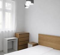 Ložnice s dřevěným nábytkem a závěsným osvětlením v dvoupokojovém bytě.