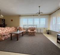 Obývací pokoj s kobercem, květovanou sedačkou a podlahou s dřevěným dekorem v rodinném domě.