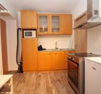 Kuchyně v 1-pokojovém bytě s podlahou s dřevěným dekorem, světlé dřevěné skříňky.