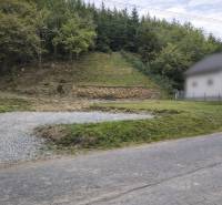 Svažitý pozemek v obci Makov s příjezdovou cestou a okolním lesním porostem. Pozemky - bydlení.