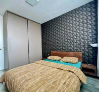 Ložnice v 2-pokojovém bytě s postelí a vzorovanou tapetou, podlaha s dřevěným dekorem.