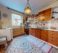 Kuchyně v rodinném domě s dřevěnými skříňkami, kobercem a závěsným svítidlem.