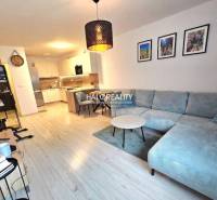 Obývací pokoj s rohovou sedačkou, kuchyní a podlahou s dřevěným dekorem v 2-pokojovém bytě.