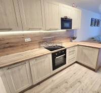 Kuchyně s podlahou s dřevěným dekorem v 2-pokojovém bytě, světlé dřevěné skříňky a vestavěné spotřebiče.