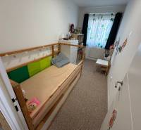 Dětský pokoj ve 4-pokojovém bytě s postelí, komodou a barevnými závěsy.