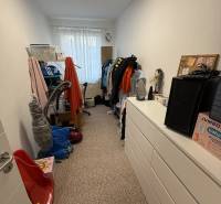 Pokoj se skříněmi a oblečením ve 4pokojovém bytě, dominují bílé stěny a koberec.