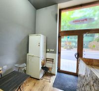 Gastro prostory s podlahou s dřevěným dekorem, lednice u stolu a vstupní dveře.