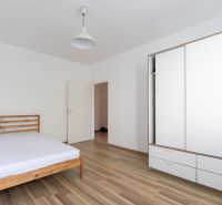 Ložnice s dřevěnou postelí, bílou skříní a podlahou s dřevěným dekorem v 3-pokojovém bytě.