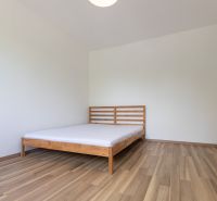 Ložnice s postelí, podlaha s dřevěným dekorem, ve 3pokojovém bytě.