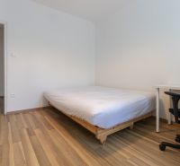 Ložnice v 3pokojovém bytě s postelí, pracovním stolem a podlahou s dřevěným dekorem.