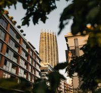 Výšková budova v pozadí ulice se zelení a bytovými jednotkami v Bratislavě.