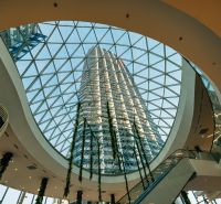 Prostorné atrium se skleněnou střechou a vysokou budovou v pozadí.