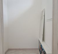 Úzká místnost s rozvaděčem v rodinném domě, světlé dlaždice, neutrální stěny.