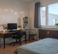 Ložnice se stolem, počítačem, židlí a regálem ve čtyřpokojovém bytě. Podlaha s dřevěným dekorem.