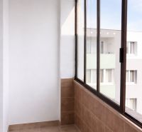 Zasklený balkon ve 4-pokojovém bytě se světlou dlažbou a výhledem na bytovku.