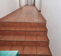 Chodba s keramickou dlažbou a schodištěm v rodinném domě.