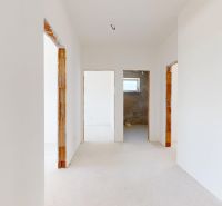 Chodba v rodinném domě s bílými stěnami a světlou podlahou s dřevěným dekorem.