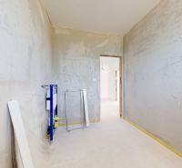 Nedokončený interiér s betonovými stěnami a prvky pro sanitární zařízení v rodinném domě.