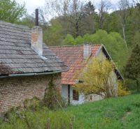 Rodinný dům v Bukovci se starou cihlovou zdí obklopený zeleným prostředím a stromy.