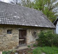 Kamenná stodola u rodinného domu v Bukovci s dřevěnými dveřmi a střešními taškami.