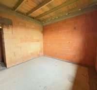 Interiér rozestavěného rodinného domu s cihlovými stěnami a betonovou podlahou.