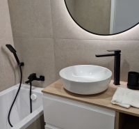 Koupelna v 3-pokojovém bytě s kruhovým zrcadlem a moderními bateriemi.