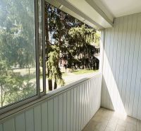Zasklený balkon ve 4-pokojovém bytě s výhledem na stromy, bílá dřevěná stěna.