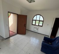 Pokoj v chatě s dveřmi na terasu, dlaždicovou podlahou a tmavomodrým křeslem.