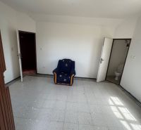 Pokoj s křeslem, bílými stěnami, dlažbou a dveřmi vedoucími na WC v chatě.
