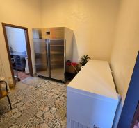 Chladicí místnost s dlažbou v gastro prostorech, obsahující kovovou skříň a mrazničku.