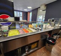 Gastro prostory s miskami, zeleninou a nápoji na pultech a podlahou s dřevěným dekorem.