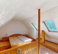 Podkrovní ložnice v rodinném domě se střešními okny a podlahou s dřevěným dekorem.