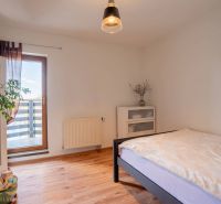 Světlá ložnice ve 4-pokojovém bytě s podlahou s dřevěným dekorem, rostlinou a balkonem.