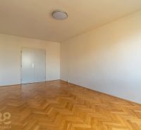 Pokoj ve 4pokojovém bytě s bílými stěnami a podlahou s dřevěným dekorem.