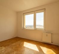Pokoj s oknem, radiátorem a podlahou s dřevěným dekorem ve 4-pokojovém bytě.