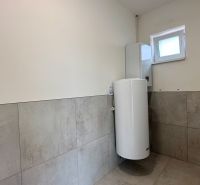 Koupelna v rodinném domě s dlaždicemi na stěnách a bojlerem.