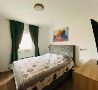 Ložnice v rekreačním apartmánu s pohodlnou postelí, dekorativním obrazem a podlahou s dřevěným dekorem.