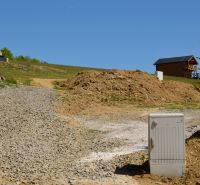 Rekreační pozemky v Nové Kelči, štěrková cesta, dřevěný dům, svahy a vegetace.