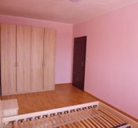 Pokoj v 2-pokojovém bytě s růžovými stěnami, skříní a podlahou s dřevěným dekorem.