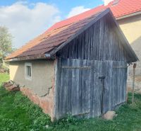 Stará dřevěná garáž na pozemku pro bydlení v Budiné, obklopená zelení a stromy.