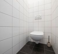 Toaleta s bílými kachličkami a černou podlahou v 2-pokojovém bytě.