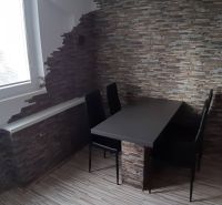 Jídelní kout se stolem a židlemi v 2-pokojovém bytě, stěna z kamene.