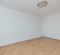 Prázdná místnost s bílými stěnami a podlahou s dřevěným dekorem ve 3-pokojovém bytě.